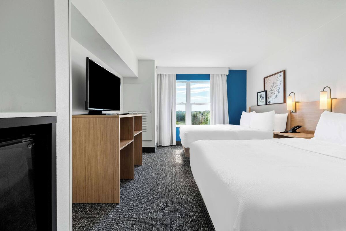 A hotel room with two beds, a TV, a desk, and a window with curtains.