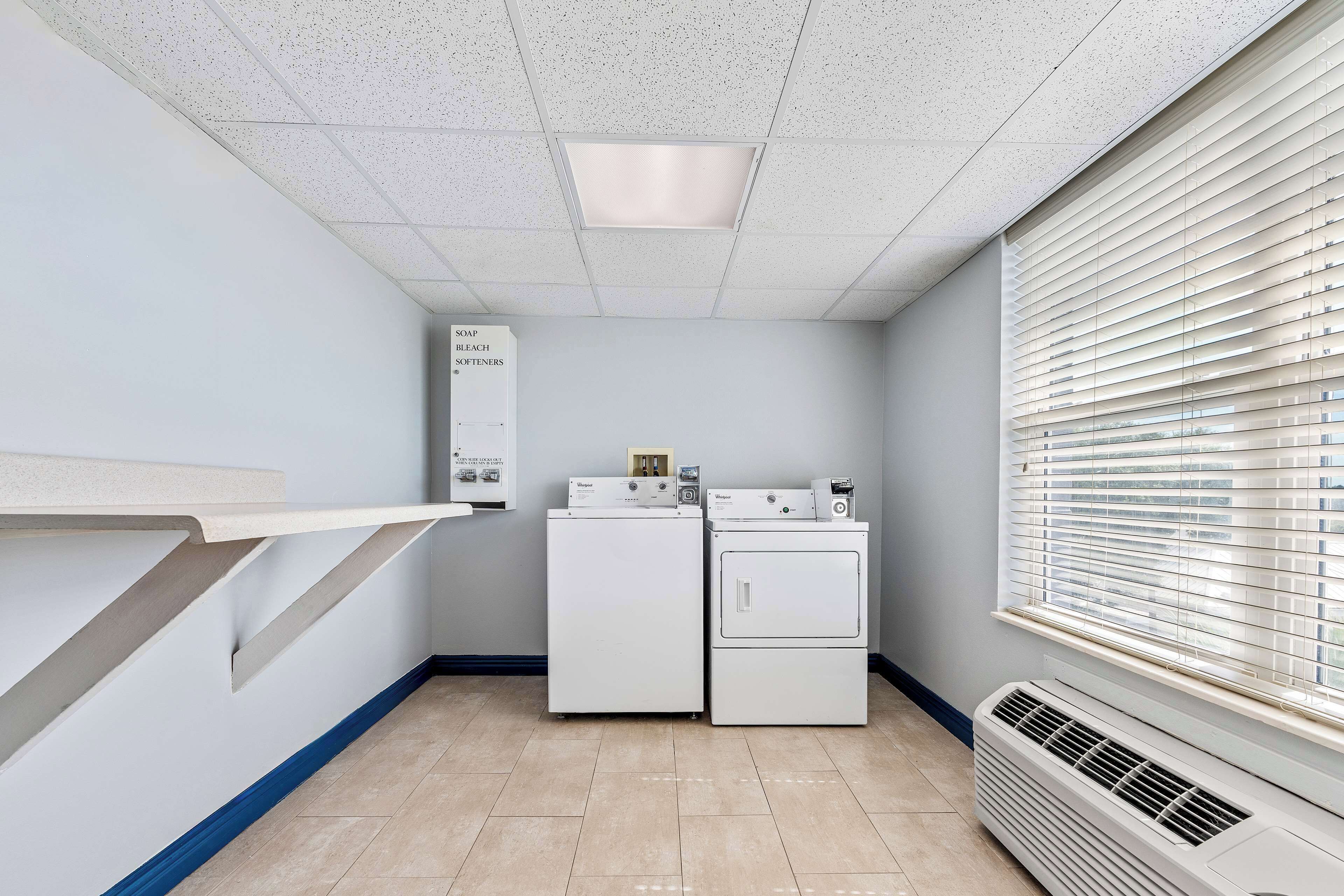 A laundry room with a wall-mounted washer and dryer, a vent, and a shelf with a soap dispenser.