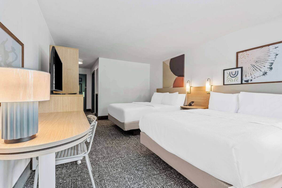A hotel room with two beds, a desk, and a chair.