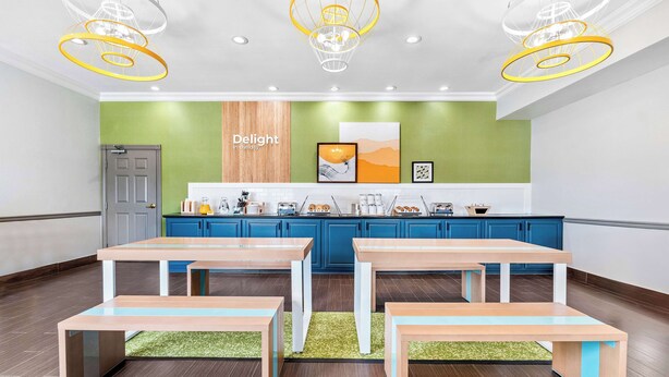 Une cuisine moderne avec deux tables et des bancs en bois, un mur d’accent vert et un panneau indiquant : « Savourez chaque instant ».