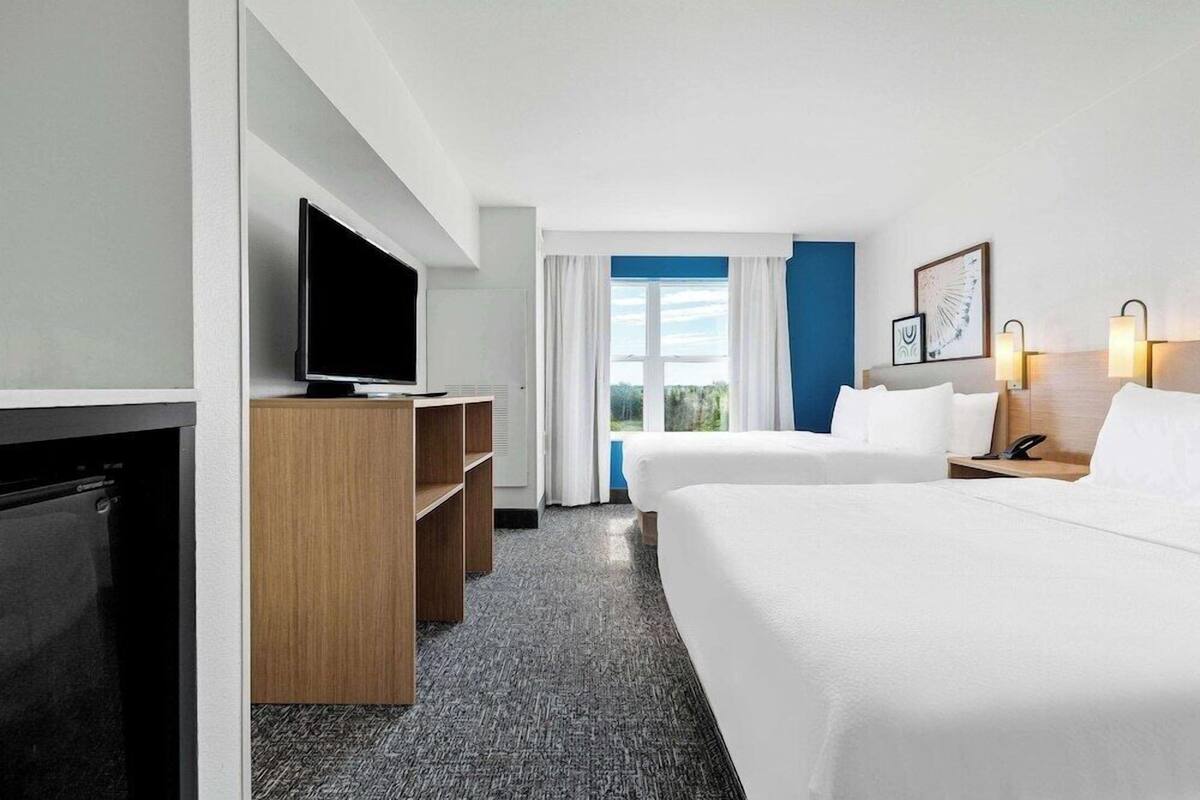 A hotel room with two beds, a TV, a desk, and a window with curtains.