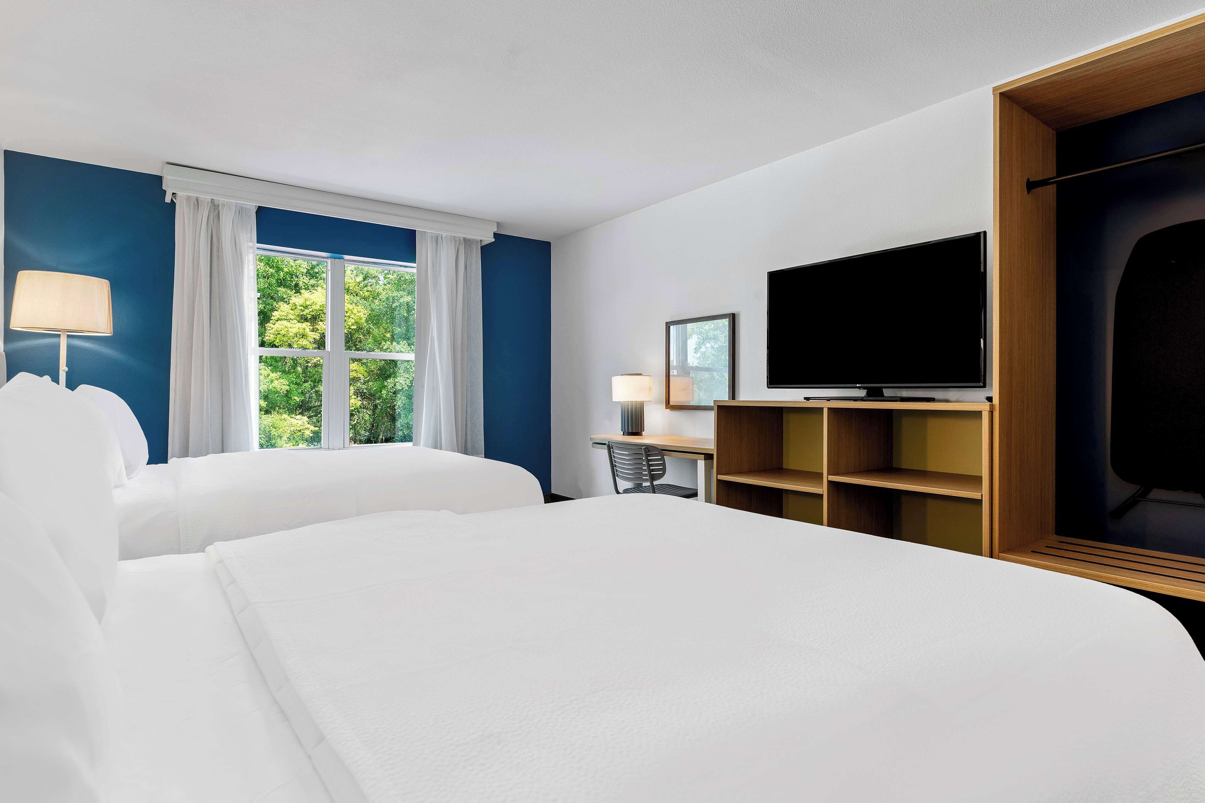 A hotel room with two beds, a desk, a TV, and a window with curtains.