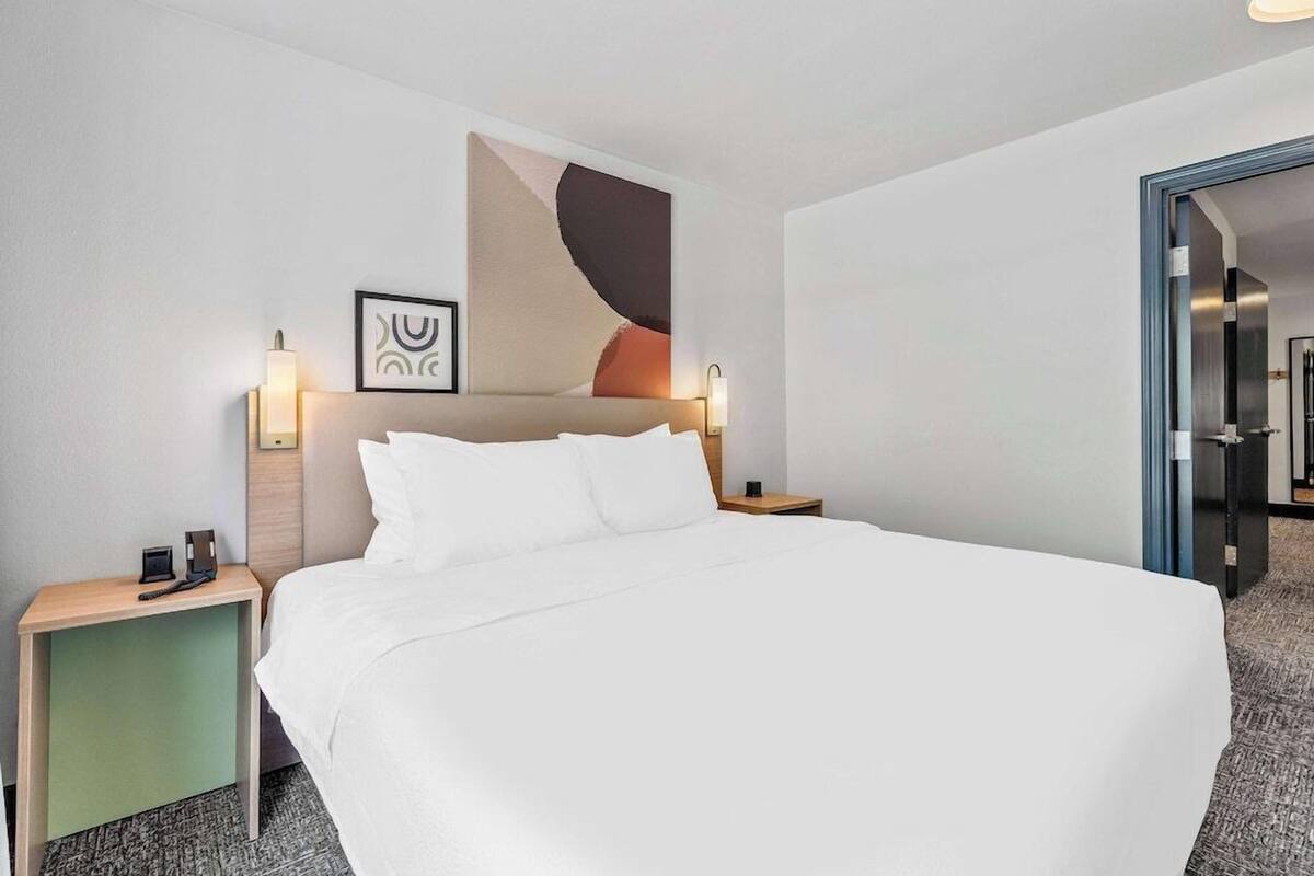 A modern hotel room with a large bed, two bedside tables, and a wall-mounted abstract painting.