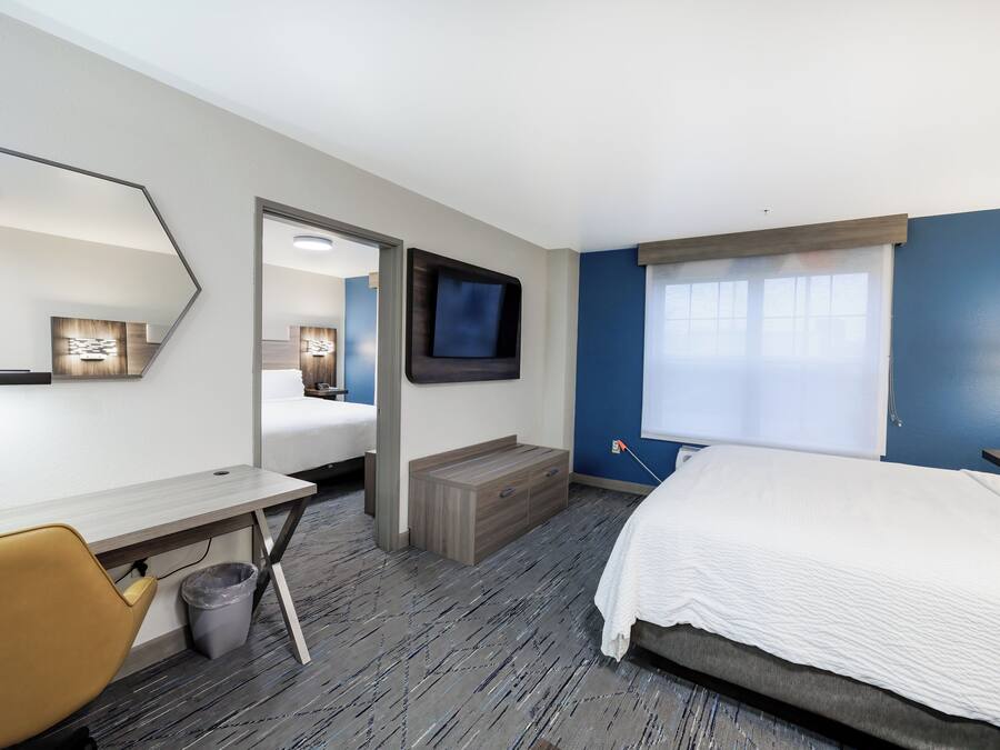 A modern hotel room with a bed, desk, chair, and a large mirror.