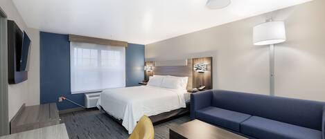 Una habitación de hotel moderna con cama, sofá, sillón, escritorio y lámpara.