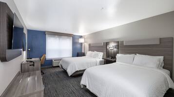 A hotel room with two beds, a desk, a chair, a bedside table, a lamp, and a large window.