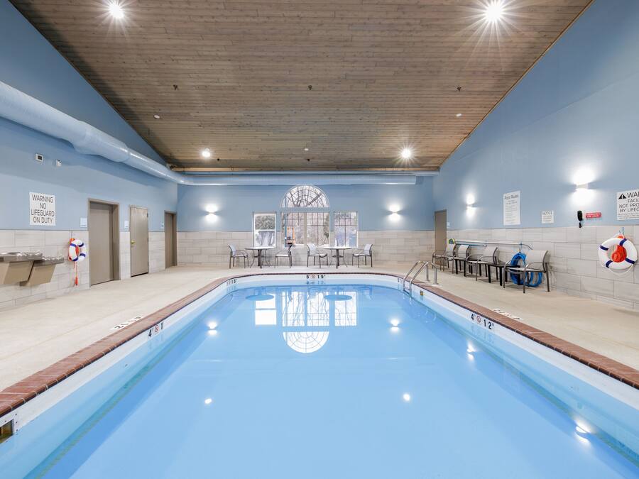 A large indoor swimming pool with a wooden ceiling, lifeguard chairs, and safety signs.
