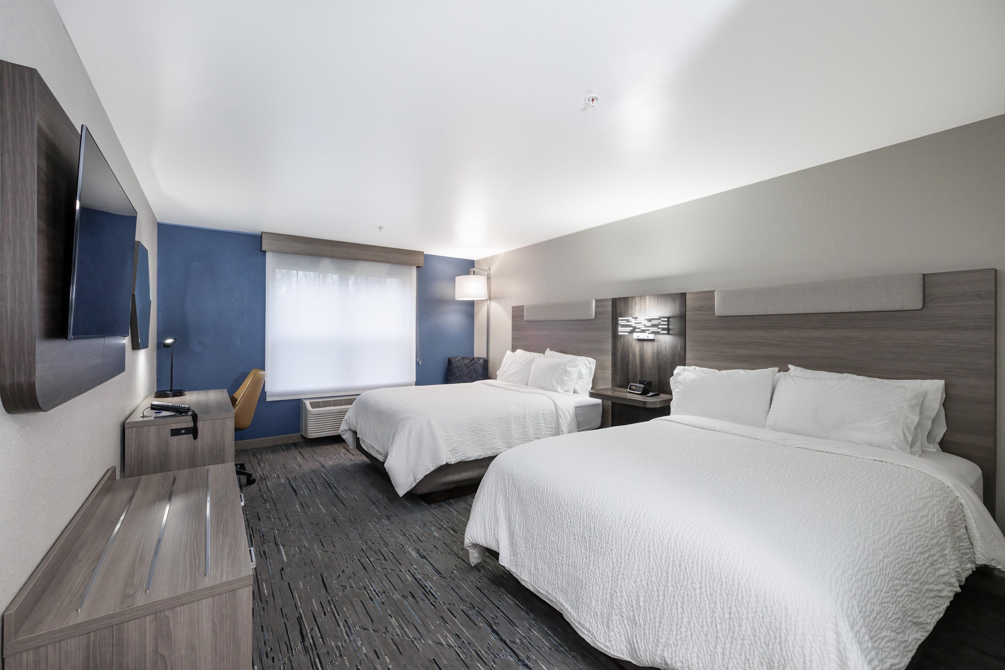 Une chambre d’hôtel avec deux lits, un bureau, une chaise, un téléviseur à écran plat et une fenêtre avec des rideaux.