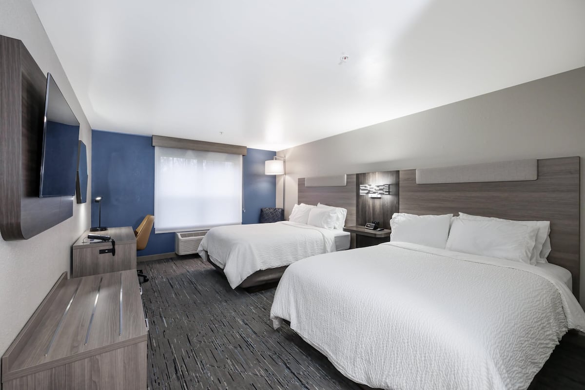 A hotel room with two beds, a desk, a chair, a flat-screen TV, and a window with curtains.