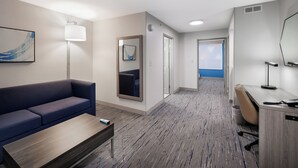 A hotel room with a blue sofa, a wooden coffee table, a desk with a chair, a large mirror, and a view of the sea through the door. - Holiday Inn Express & Suites Zion by IHG (Zion)