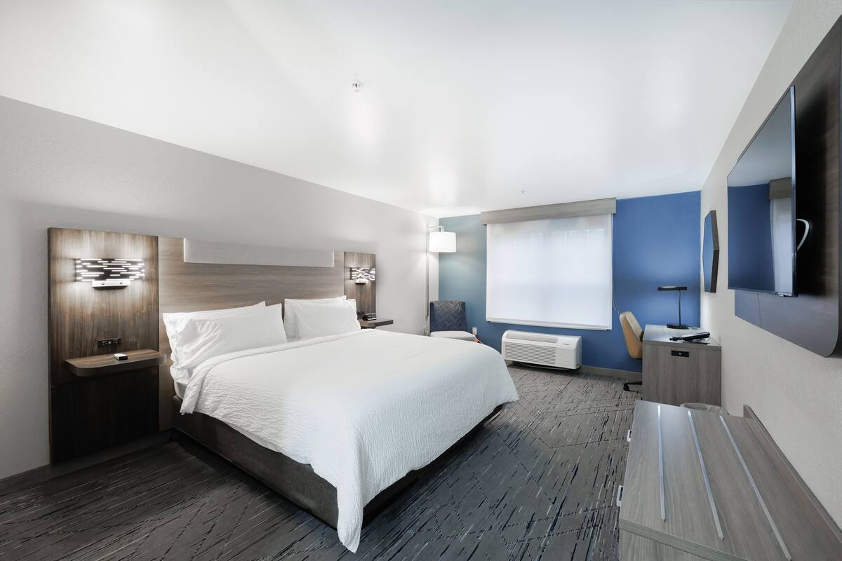 A modern hotel room with a large bed, a desk, and a TV.