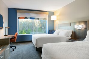 A hotel room with two beds, a desk, and a chair. There is a large window providing a view of trees.