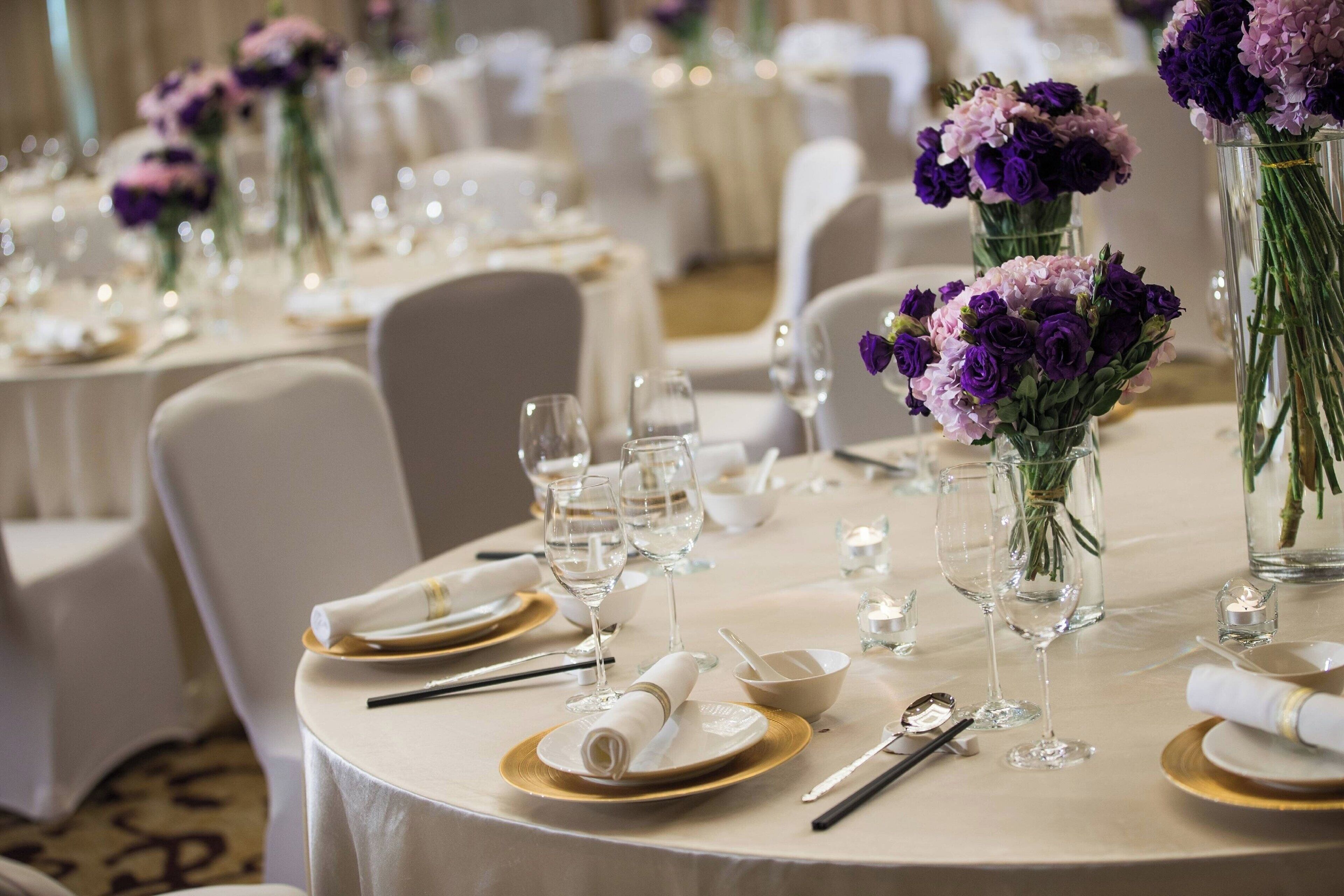 A banquet table set with white tablecloths, gold-rimmed plates, and clear glassware.