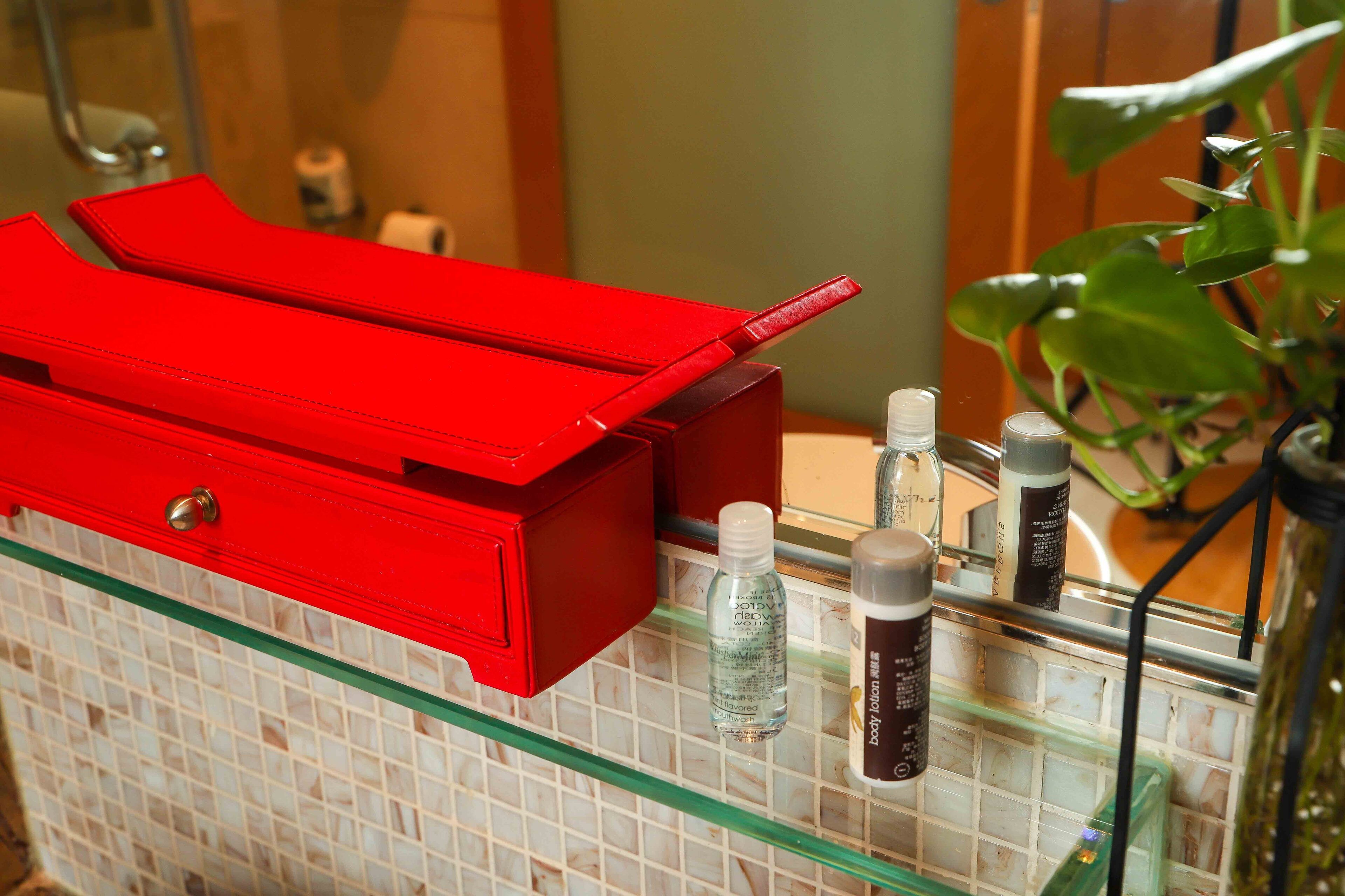 A bathroom with a red cabinet, a glass shelf, and toiletries.