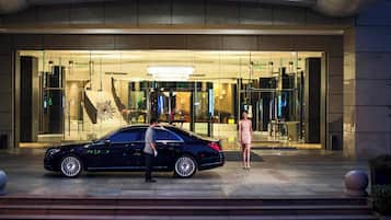 A black car parked in front of a building with a glass entrance, a staircase, and a chandelier.