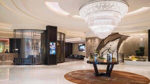 Eine geräumige Lobby mit einem großen Kronleuchter, einem Empfangstresen und einer modernen Treppe.