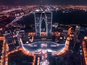 Un grand bâtiment moderne, doté d’une structure arquée remarquable et d’une vaste place illuminée devant l’entrée.