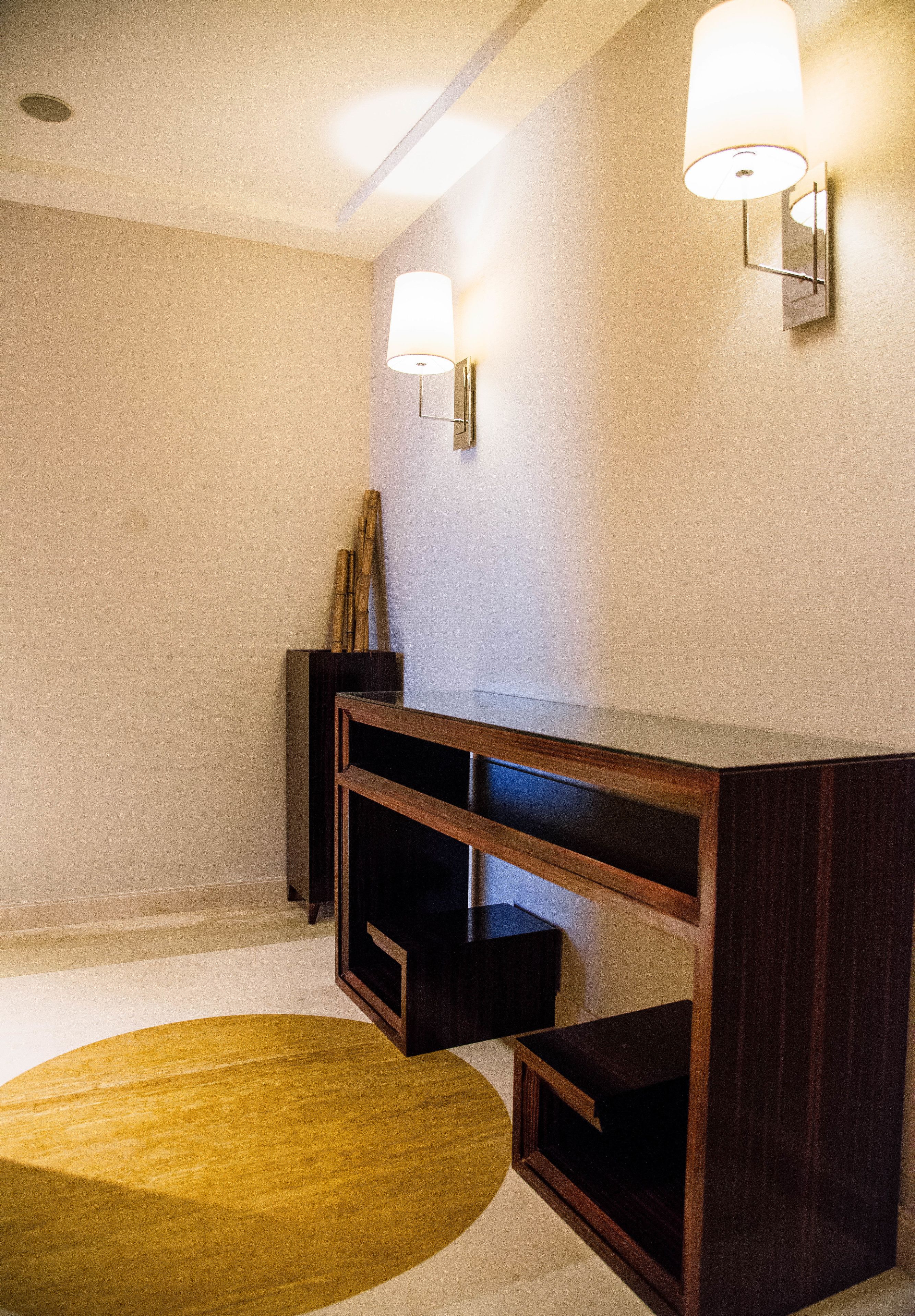 A hallway with a wooden console table, two wall-mounted light fixtures, and a round yellow rug.