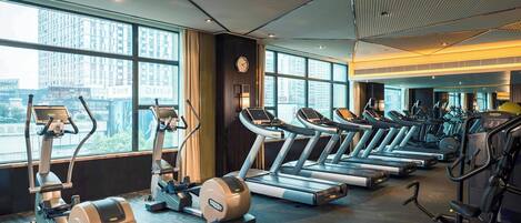 Un gimnasio con cintas de correr, elípticas y bicicletas estáticas, amplias ventanas y un diseño moderno de techo.