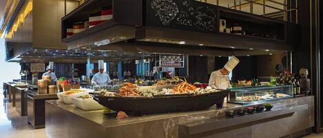 A modern restaurant with a sushi bar, chefs preparing food, and a variety of dishes displayed.