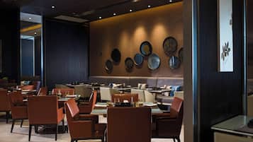 Un restaurante moderno con varias mesas y sillas, una pared decorada con platos y un panel de madera oscura a la derecha.