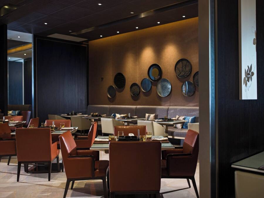Un restaurante moderno con varias mesas y sillas, una pared decorada con platos y un panel de madera oscura a la derecha.