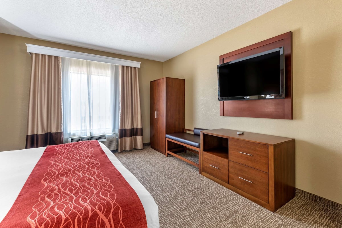 A hotel room with a bed, a TV mounted on the wall, a wooden cabinet, and a window with curtains.