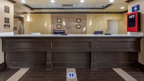 Un área de recepción con un mostrador de madera oscura, un logotipo grande montado en la pared y un quiosco informativo rojo.