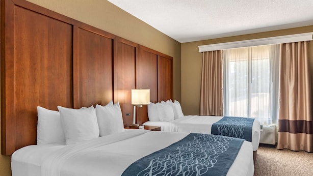Habitación de hotel con dos camas, cabecera de madera, paredes color beige y un ventanal con cortinas.
