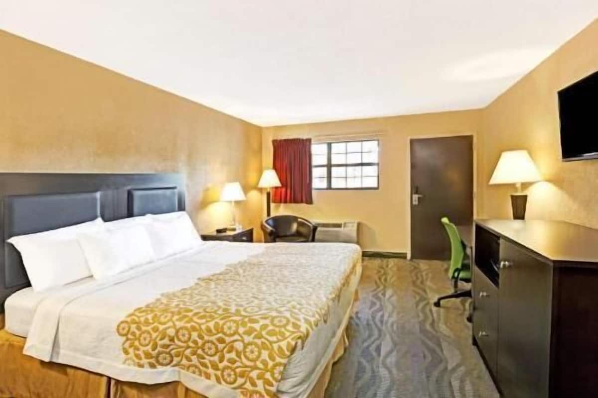 A hotel room with a bed, two bedside tables with lamps, a chair, a desk, a television, and a window with curtains.