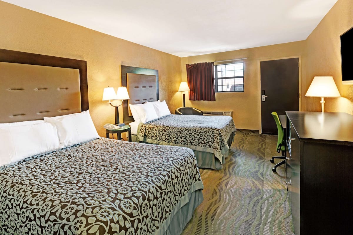 A hotel room with two beds, a desk, a chair, and a television.