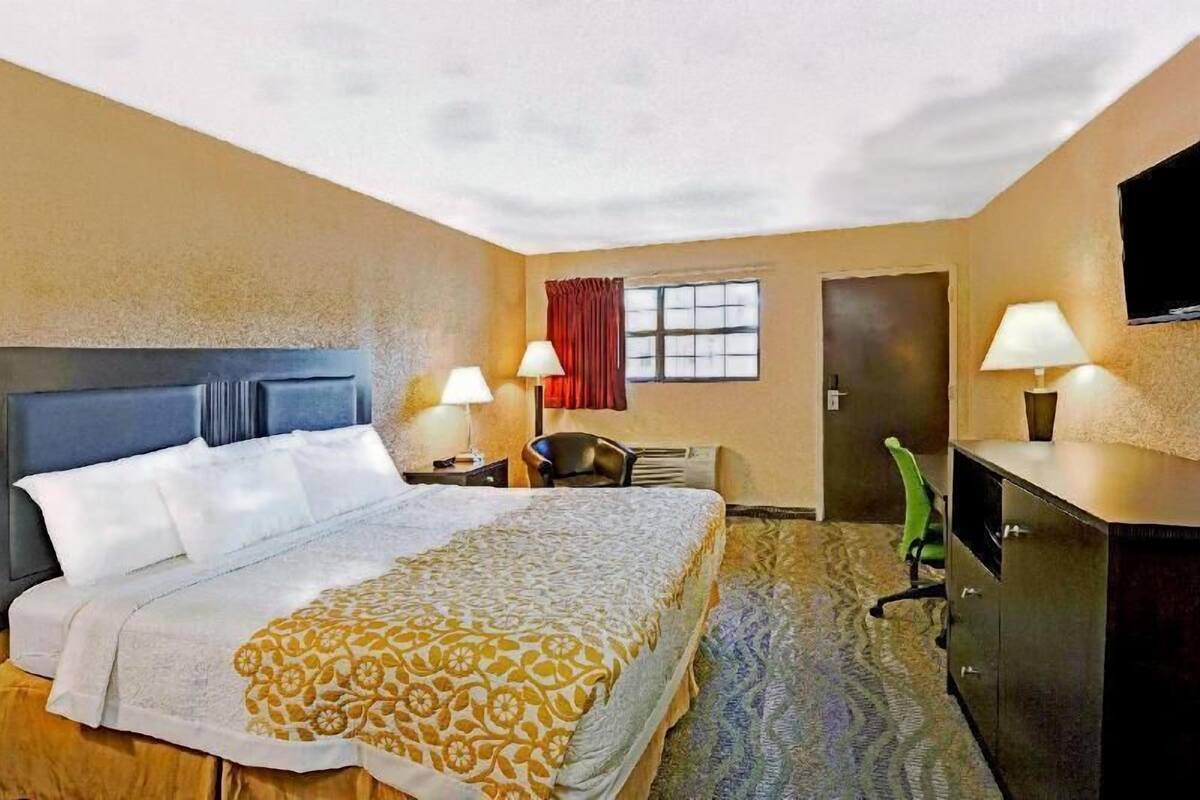 A hotel room with a bed, two bedside lamps, a desk, a chair, a television, and a door.
