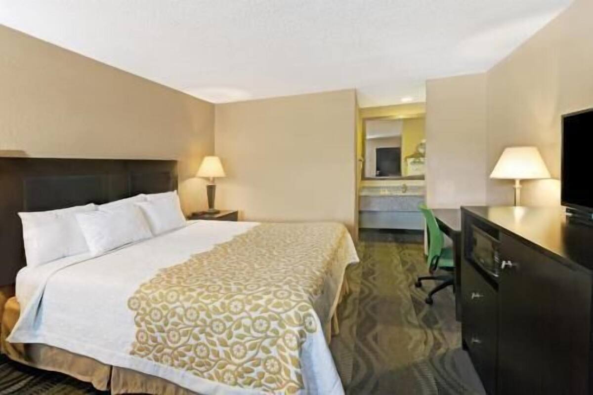 A hotel room with a bed, two bedside lamps, a desk with a television, and a mirror.