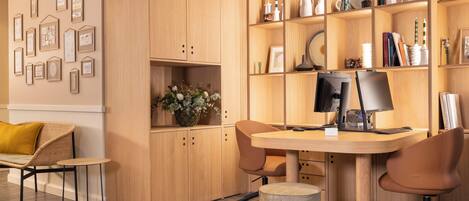 A modern office space with a wooden desk, two chairs, a computer, and a bookshelf filled with books and decorative items.