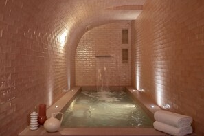A spa area with a brick wall, a hot tub, and towels. - Le Petit Oberkampf Hotel & Spa (Paris)