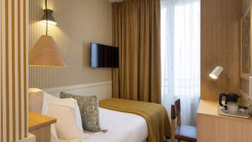 Una habitación de hotel con cama, escritorio con lámpara, televisor y ventana con cortinas.