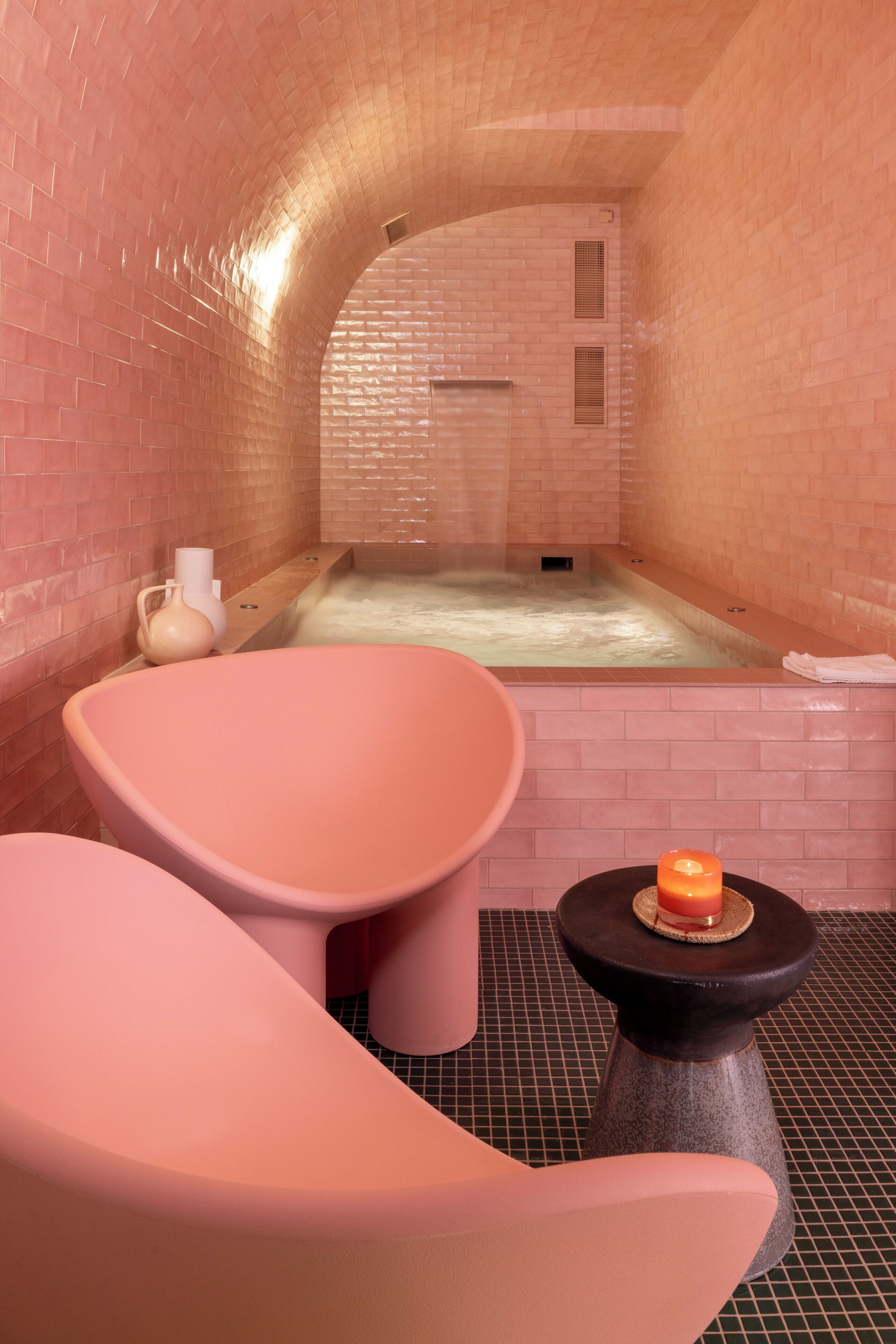 A spa room with a brick wall, a bathtub, and two pink chairs.