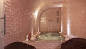Un área de spa con pared de ladrillo, un jacuzzi y dos sillones de mimbre.