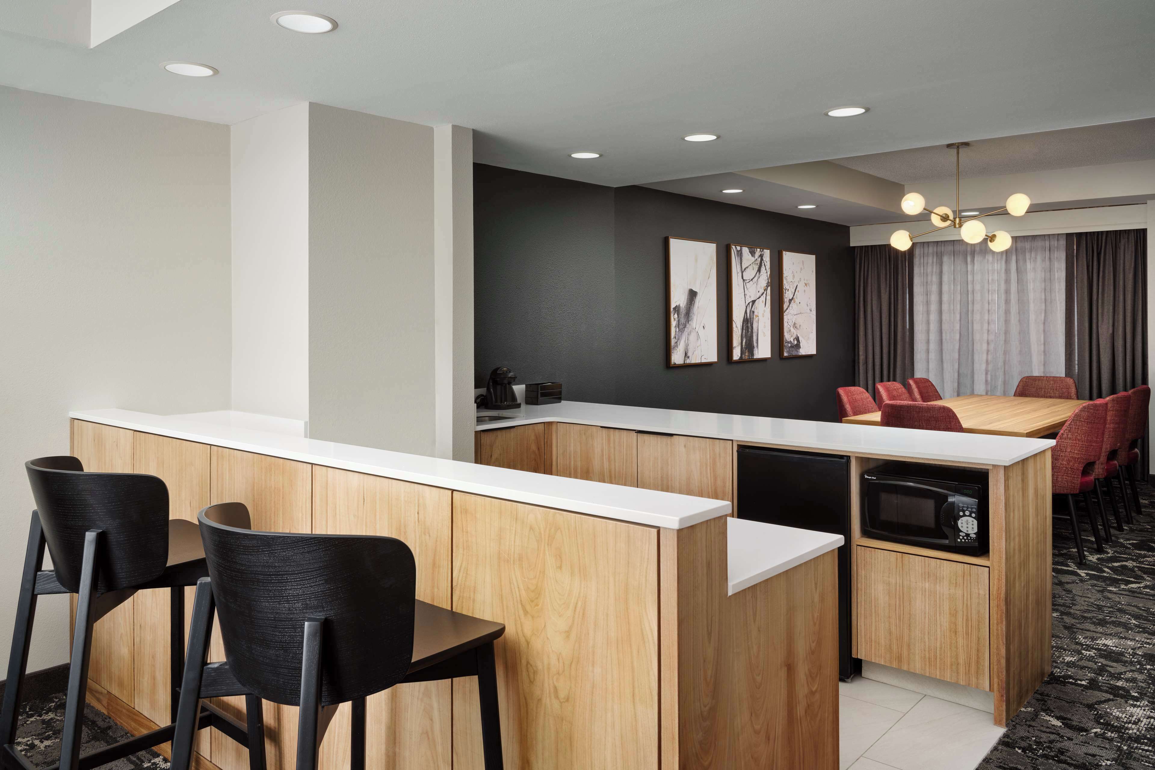 A modern kitchen with a central island, bar stools, a dining table with red chairs, and a microwave.