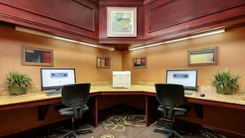 A hotel office with two desks, two chairs, a printer, and two potted plants.