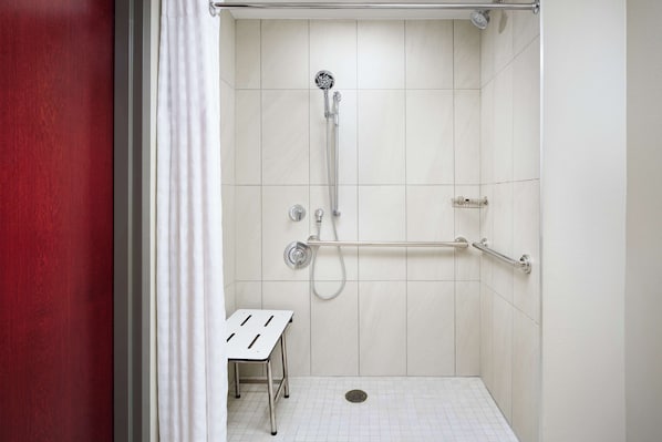 A walk-in shower with a handheld showerhead, grab bars, and a bench.