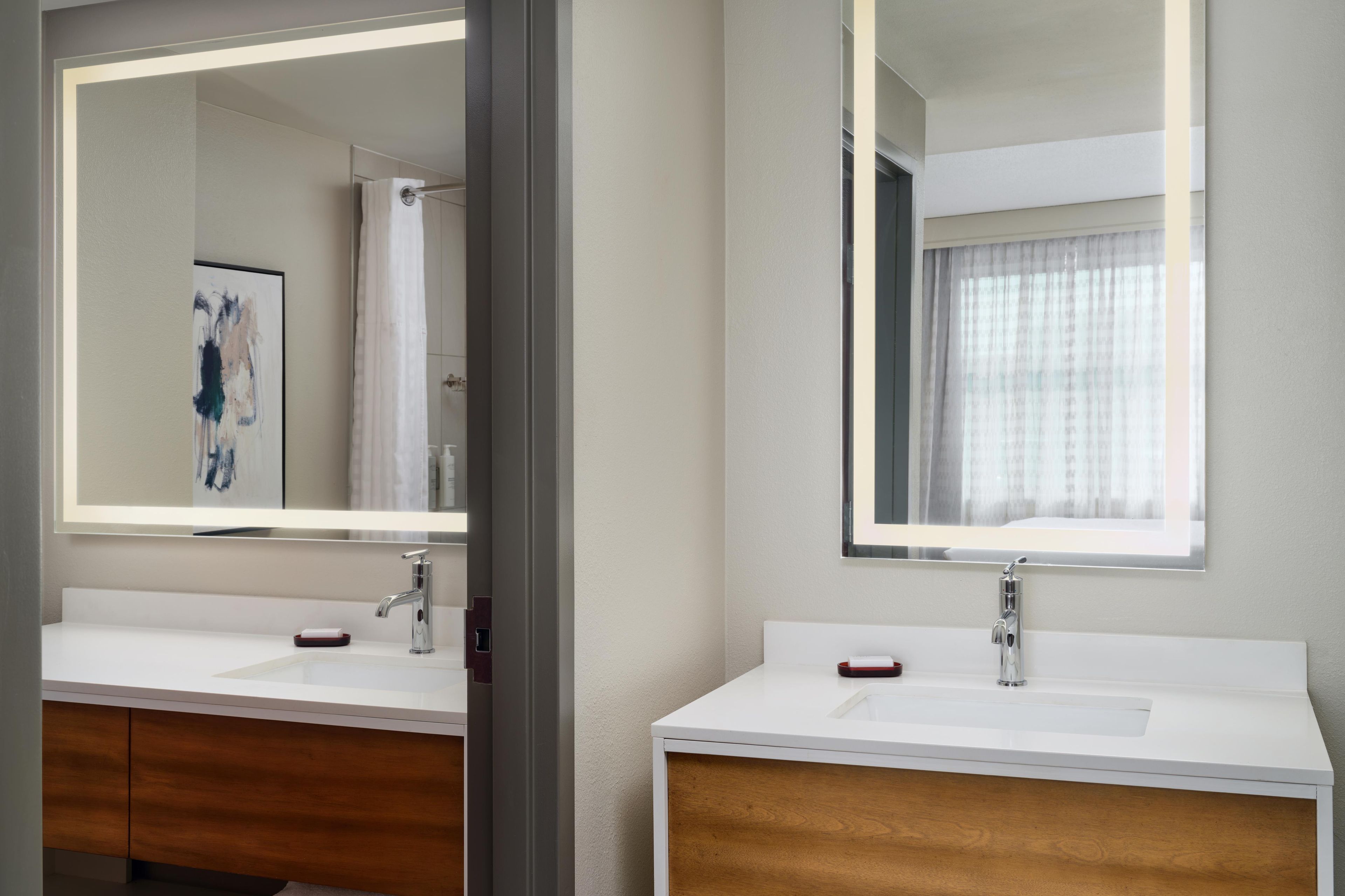 A hotel bathroom with two sinks, a mirror, and a shower.