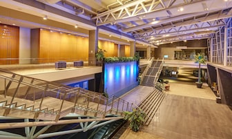 Un vestíbulo de hotel con una escalera monumental, una recepción y una zona de estar con sillas.