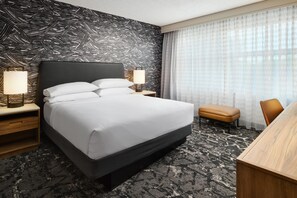 A hotel room with a bed, bedside tables, a lamp, a bench, and a view of the outside through a window.