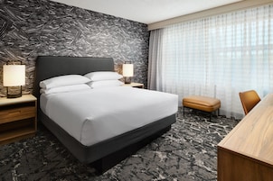 Habitación de hotel con cama, mesitas de noche, lámpara, una banca y vistas al exterior a través de una ventana.