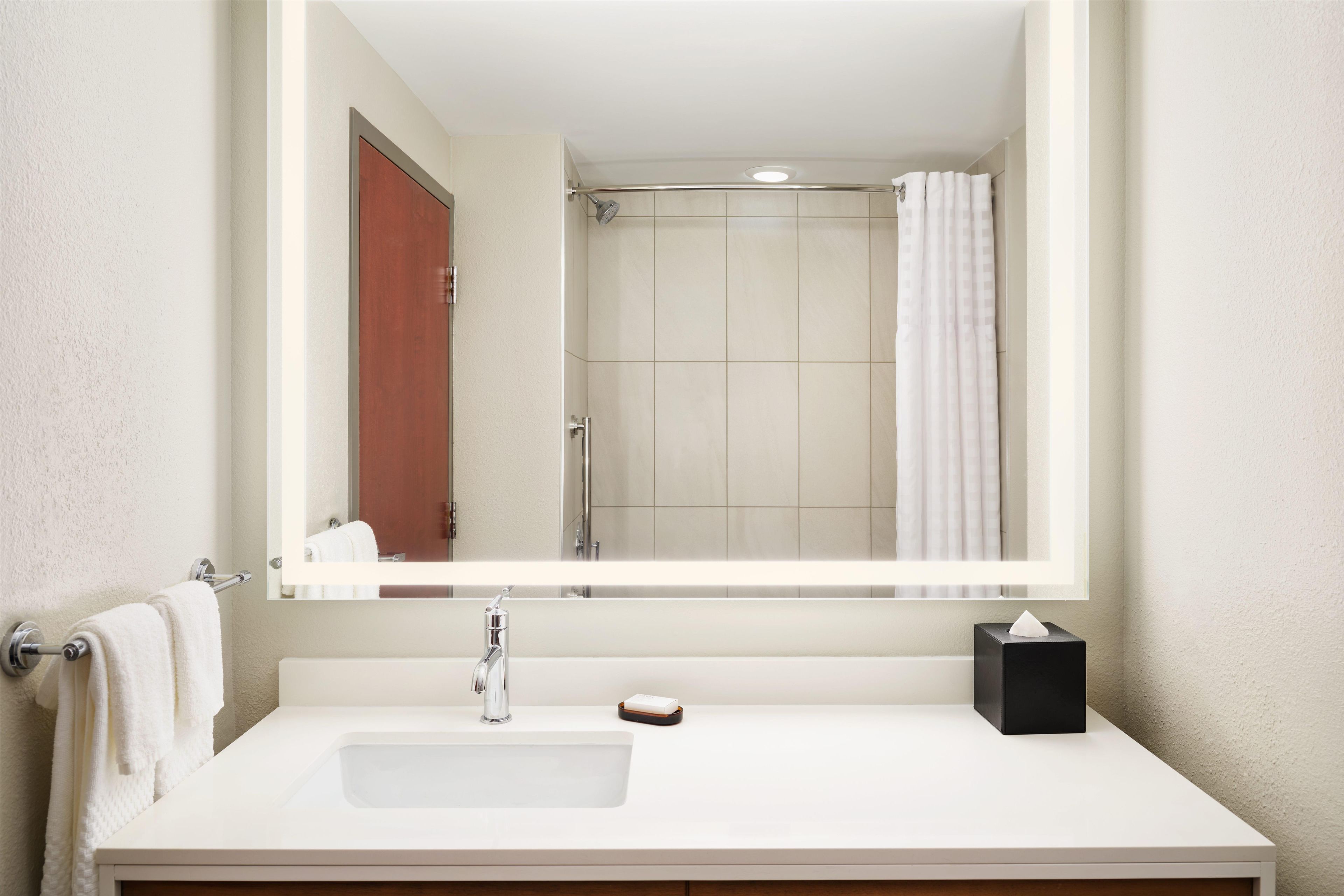 Un baño con lavamanos blanco, un espejo, toallero y zona de ducha.