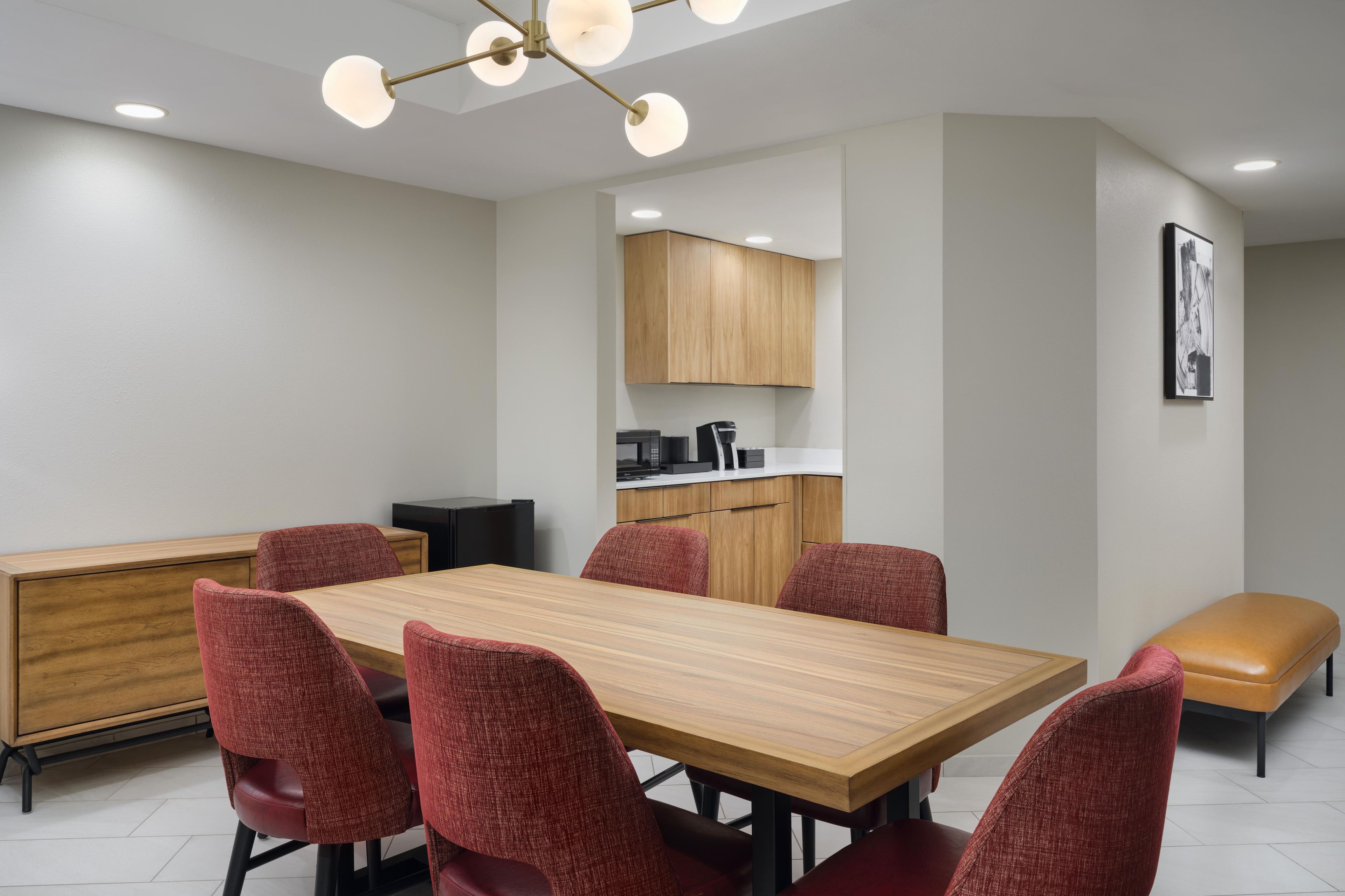 Un comedor moderno con una mesa de madera y sillas tapizadas rojas, una cocina al fondo y un banco con cojín.