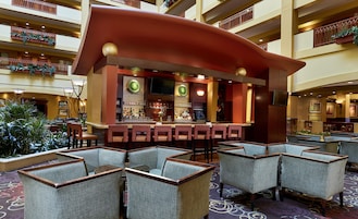 Un vestíbulo de hotel con una zona de bar curva, asientos y vistas de los pisos superiores.