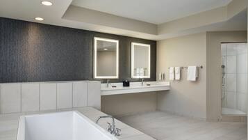 A modern bathroom with a large bathtub, two sinks, a walk-in shower, and a textured wall.