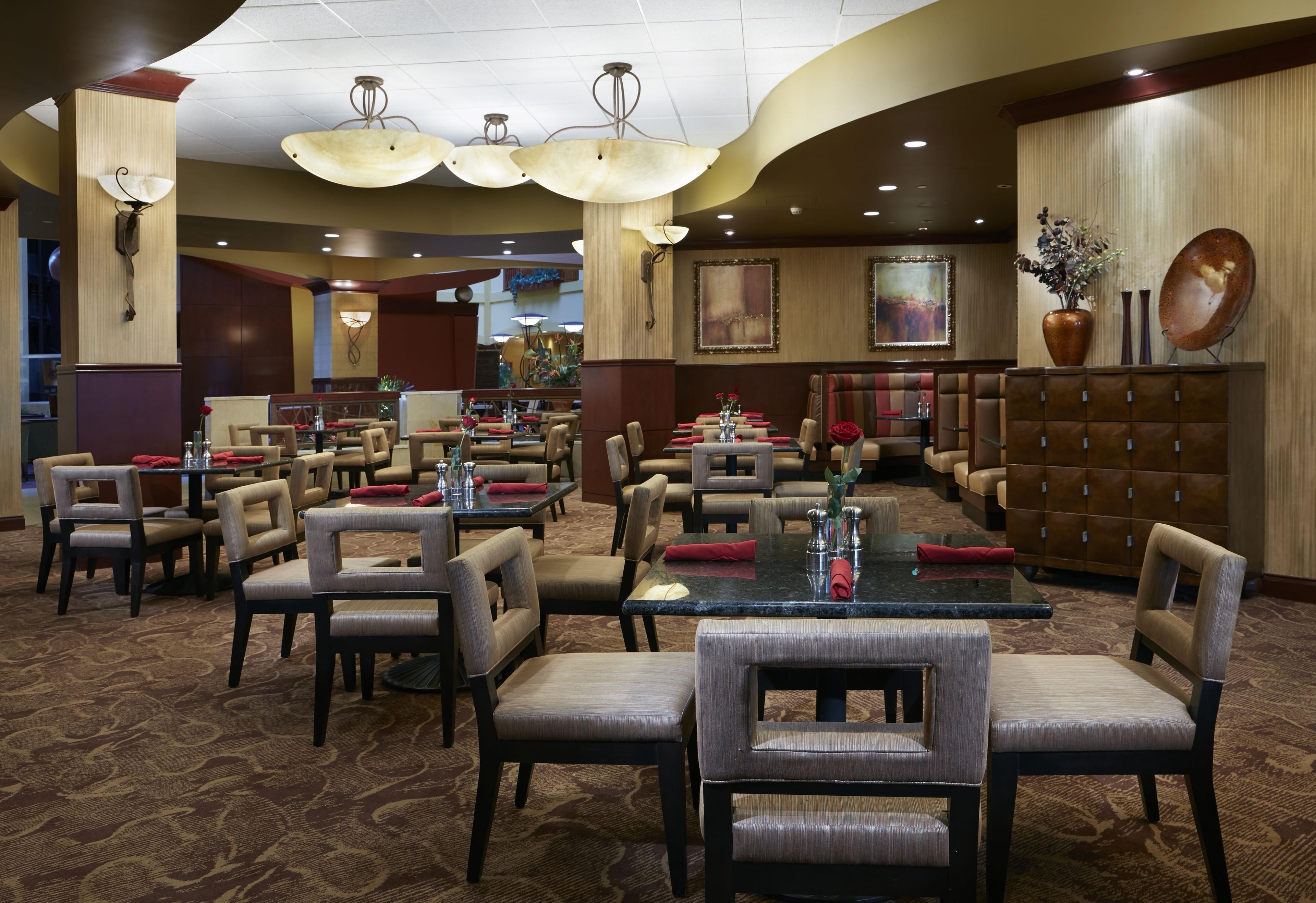 A hotel dining area with multiple tables and chairs, decorative lighting, and artwork on the walls.